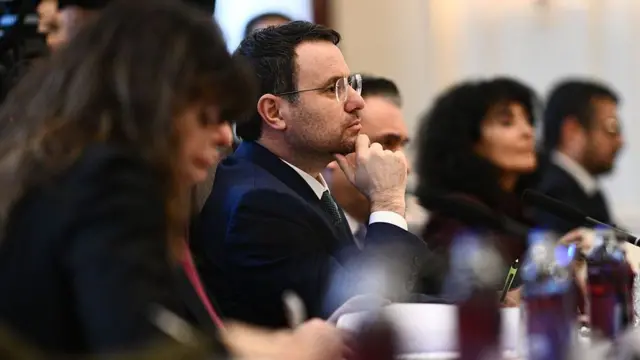 Akın Gürlek yandan görünüyor masada odakta. 